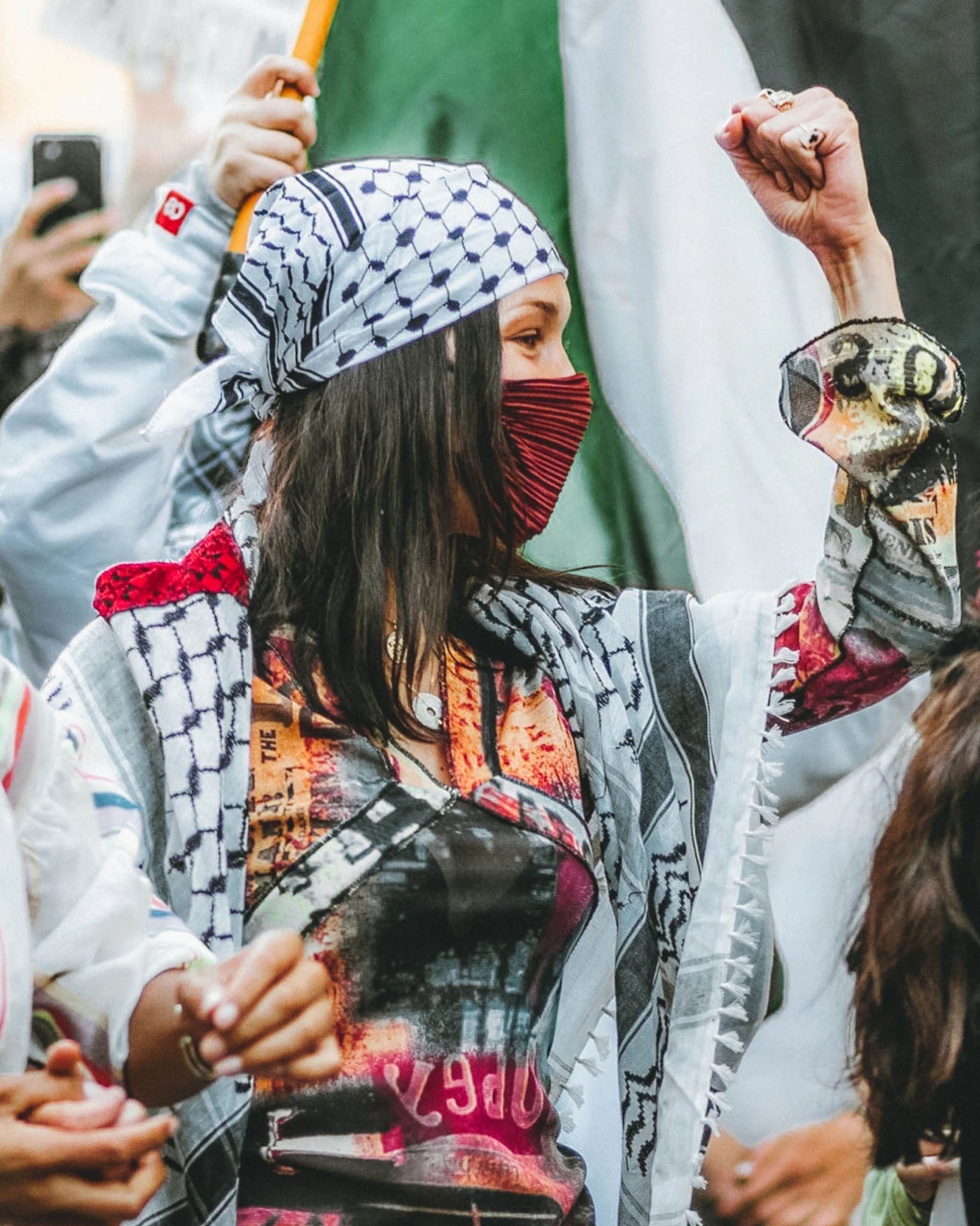 Bella Hadid in a scarf and a kufiya bandana raises a flag, symbolizing her enthusiasm and commitment to the Palestinian movement.