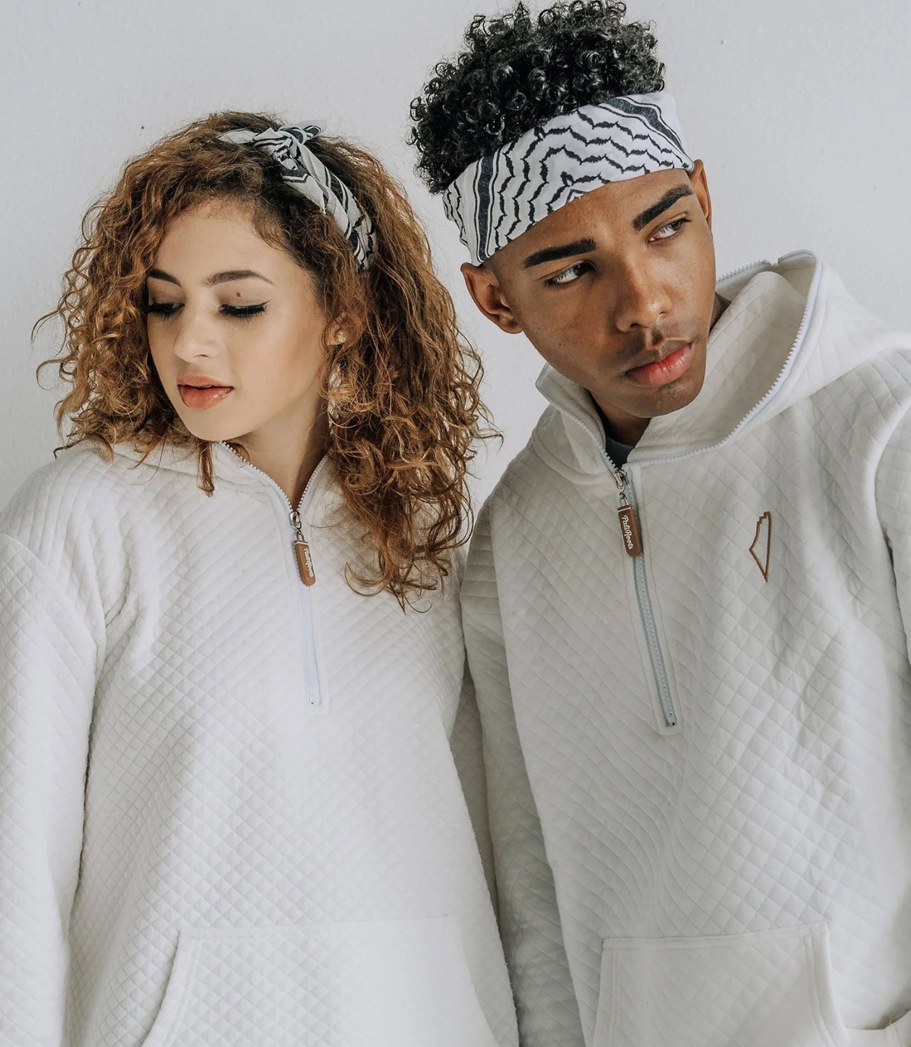 Two young people wearing matching white sweatshirts and Kufiya bandanas in their heads, posing for the camera.